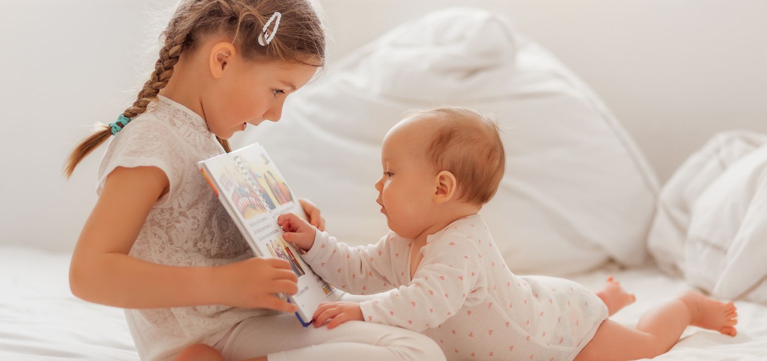 A young girl and a baby reading a book.