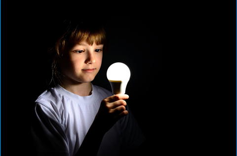 A photo of a teen looking at a lit lightbulb.
