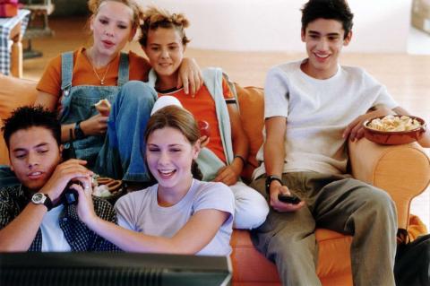 A group of teens watching a movie on a couch.